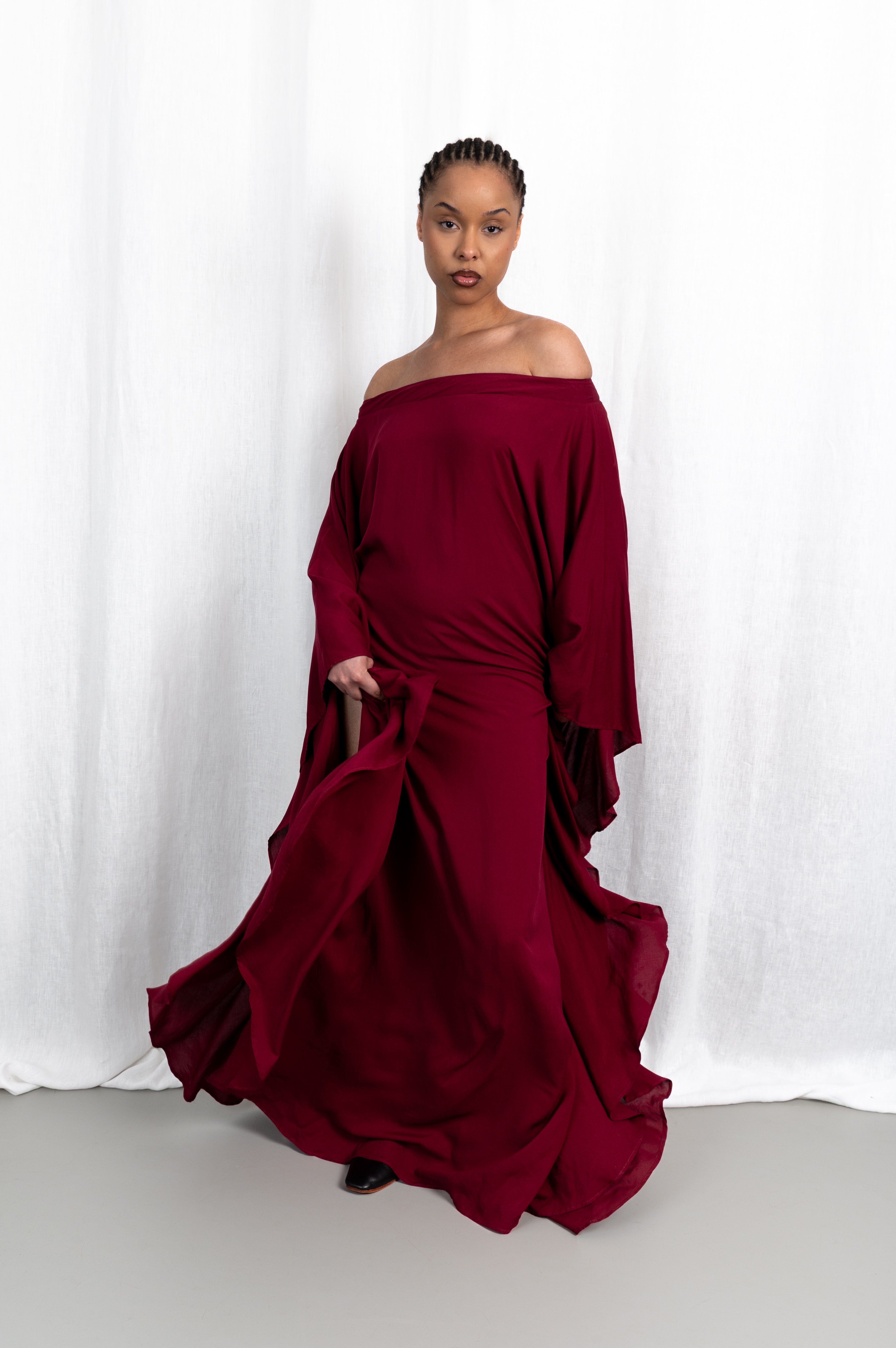 Modèle portant la robe Aduna aux épaules dénudées, vue en mouvement #couleur_bordeaux profond